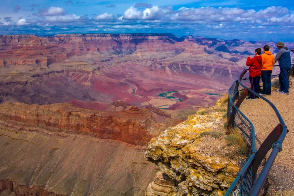 Two children and an adult looking out over railing at Grand Canyon.